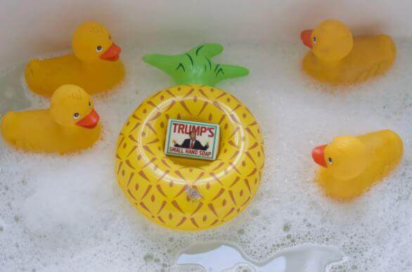 Four rubber ducks float around Danna Bananas' "Trump's Small Hand Soap," shaped like a pineapple, in a bubbly bath. The cucumber olive oil scent adds a fresh twist, making it one of those funny gifts sure to spark laughs and surprise.