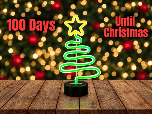 Glowing green neon Christmas tree light on a wooden table with text reading 100 Days Until Christmas
