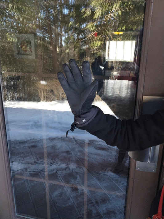 A gloved hand pressed against a glass door on a snowy winter day, reflecting on Groundhog Day predictions and the changing of seasons.