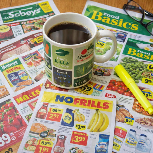 Canadian grocery flyers with coffee mug and highlighter on kitchen table