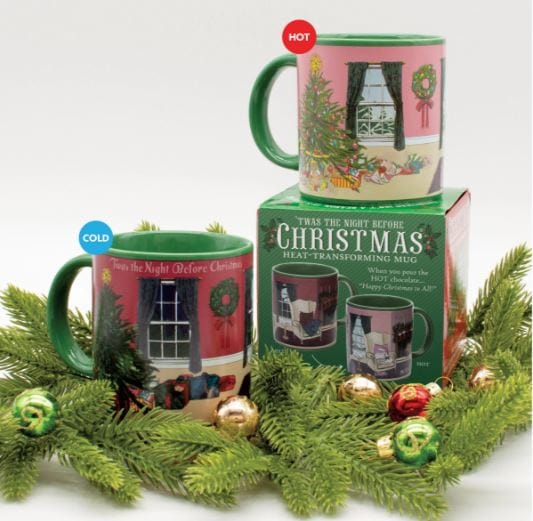 Two Twas the Night before Christmas Heat-Changing Mugs by Danna Bananas, one labeled "cold" and the other "hot," are placed beside a festive packaging box. Surrounded by pine branches and ornaments, these mugs make an ideal holiday gift as their design transforms with temperature.
