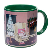 The Twas the Night before Christmas Heat-Changing Mug from Danna Bananas is a festive holiday gift, featuring a cozy scene of Santa relaxing with a cat. The mug has a green handle and, when heated, reveals an illustration of a decorated fireplace, stockings, and candles by a snowy window, adding magic to your celebrations.