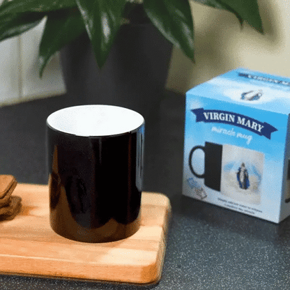 a black Virgin Mary Miracle mug on a wooden tray next to a box of cookies. with the Virgin Mary Miracle Mug behind it