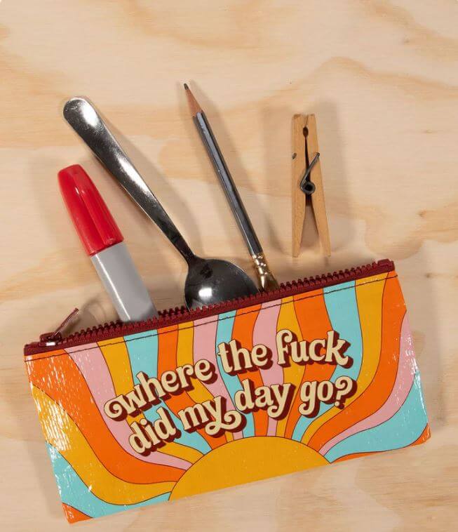 Blue Q Where’d My Day Go pencil case holding a pencil, marker, spoon and wooden clothespin on a light wood surface.