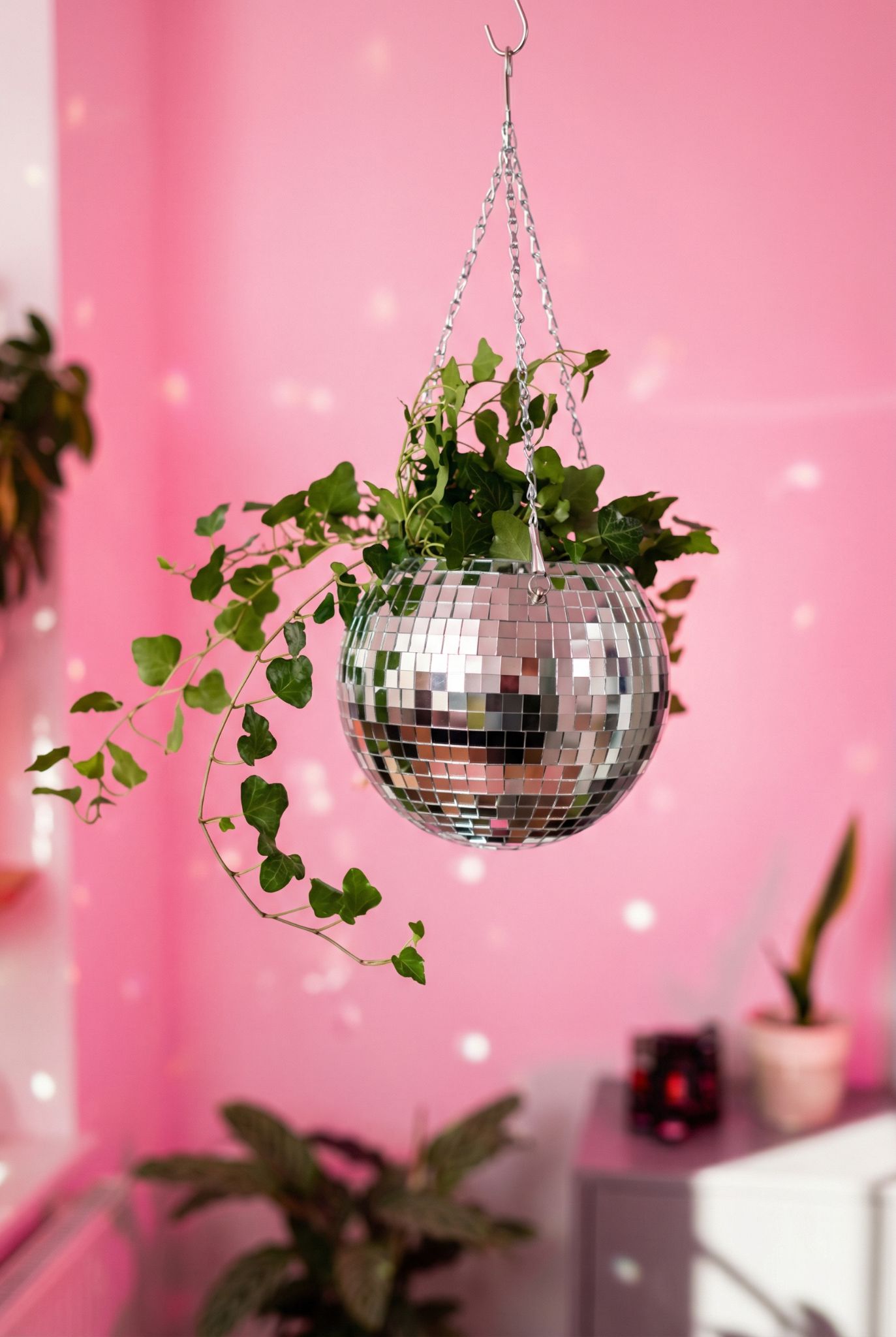 Silver disco ball hanging planter with trailing ivy against a bright pink background creating a retro spring party vibe for home décor and gift inspiration.