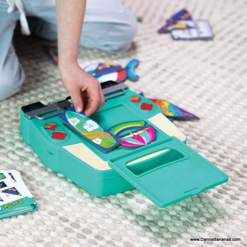 Close-up of a person engaged with the Road Trip Packing Puzzle from Outset Media on a carpet. The green puzzle, featuring colorful pieces, has buttons and a small flap. The person's hand is skillfully placing a piece, enhancing spatial reasoning skills.