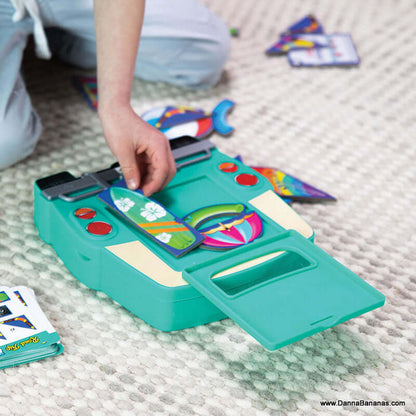 Close-up of a person engaged with the Road Trip Packing Puzzle from Outset Media on a carpet. The green puzzle, featuring colorful pieces, has buttons and a small flap. The person's hand is skillfully placing a piece, enhancing spatial reasoning skills.