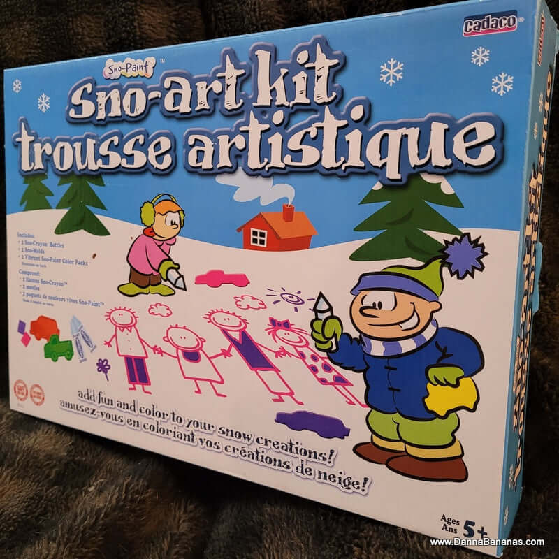 The Sno-Art Kit by Danna Bananas features cartoon characters and vibrant paint packs. It includes colorful shapes for frosty creations, with descriptions in French and English. Suitable for ages five and up.
