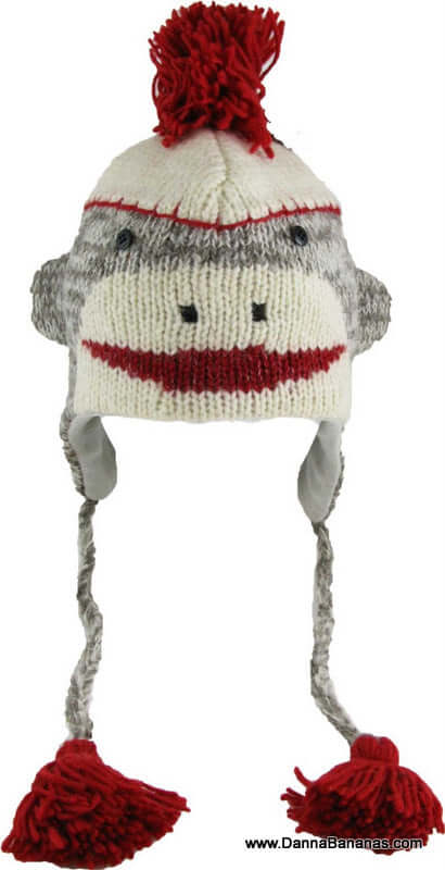 The Sock Monkey Pilot Hat - Grey Adult by Danna Bananas is crafted from soft New Zealand wool, featuring a playful monkey face with a red smile, a red pom-pom, and long braided tassels, all made using fair trade practices.