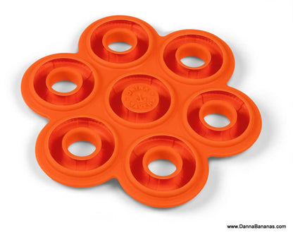 A quirky Drink Saver from World Wide Fred, featuring an orange, flower-shaped design with six rounded slots perfect for holding bottles or cans. This unique item includes raised circular ridges and has "drink saver" embossed in the center. The bottom right corner displays the website "www.DannaBananas.com", echoing the playful style of World Wide Fred.