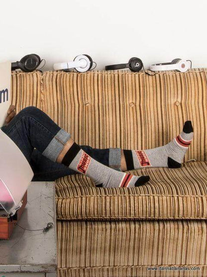 On a striped sofa, a music-loving dad shows off his Giant Music Snob Men's Crew Socks by Danna Bananas beneath rolled-up jeans. Nearby, headphones eagerly await the next playlist session.