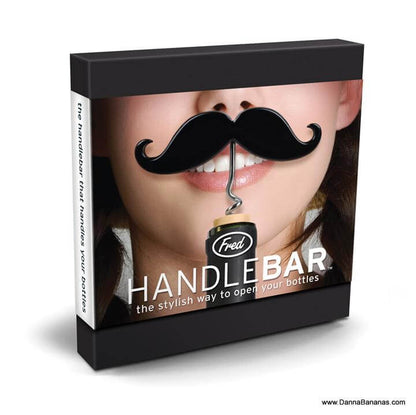 A product box showcasing a Handlebar Corkscrew & Bottle Opener designed as a black handlebar mustache. Positioned as if the mustache is on the person's face. Text on the box reads: "Fred HANDLEBAR—the stylish way to open your bottles." Perfect for Movember Canada enthusiasts! Website: www.DannaBananas.com by Danna Bananas.