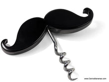 A Handlebar Corkscrew & Bottle Opener from Danna Bananas, featuring a black mustache-shaped design with a shiny silver spiral, is laying on a white surface. It combines functionality with a playful, quirky look, reminiscent of Movember Canada.