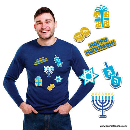 A cheerful man dons the Hanukkah Instant Ugly Sweater Kit by Danna Bananas, featuring vibrant Hanukkah-themed graphics including a menorah, Star of David, dreidels, coins, and a gift. The text "Happy Hanukkah!" is highlighted with festive embroidered patches for an extra holiday flair.