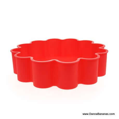 The Danna Bananas I Heart Cake Mold is a red, flower-shaped silicone mold with wavy edges, ideal for baking or shaping food items. It features a non-stick surface and is displayed against a plain white background.