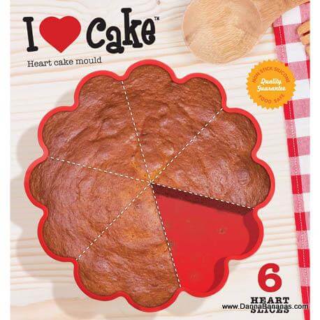 Top view of a partially sliced heart-shaped cake in the red, non-stick I Heart Cake Mold by Danna Bananas with "I ♥ cake" above it. A checkered cloth and wooden utensils appear slightly on the right.