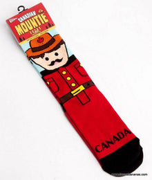 A pair of Danna Bananas Canadian Mountie Socks featuring the design of a Canadian Mountie uniform, with a red jacket, belt, and hat. The packaging at the top reads "Canadian Mounted Police Socks" with a maple leaf graphic. The word "Canada" is printed near the toe area. One size fits most.