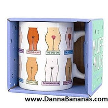 The Muff Mug by Danna Bananas is packaged in a box with cartoon illustrations of women's torsos showcasing diverse female pubic hairstyles humorously labeled, partially visible packaging adds to its quirky charm.