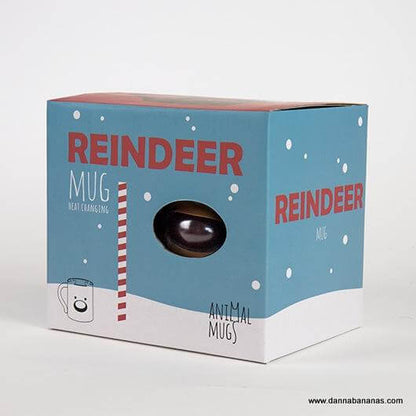 The packaging box, in blue and white, highlights the Reindeer Heat Change Mug from Danna Bananas, making it an ideal Secret Santa gift. It includes red text and a small window that displays part of the mug inside, decorated with snowflakes and candy cane motifs.