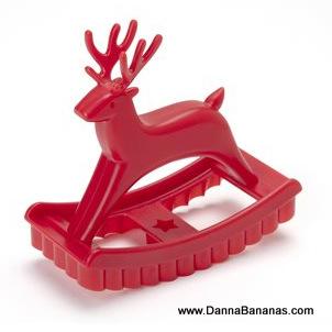 A vibrant red plastic Sweet Deer Cookie Cutter by Danna Bananas, designed as a charming reindeer on a rocker base, ideal for crafting festive cookies. The rocker base showcases a ridged edge and an adorable star-shaped cutout, making it perfect for any sugar cookie recipe. The website "www.DannaBananas.com" appears in the bottom right corner.