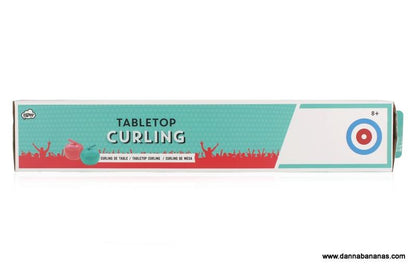 Box for the Danna Bananas Tabletop Curling Game, showcasing a blue and red design with curling graphics on the curling sheet. The text specifies that it is suitable for ages 8 and up. The box displays the brand logo and website URL.
