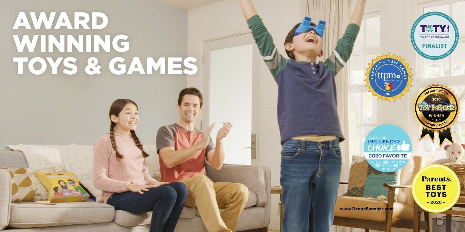 In the cozy living room, a joyful family revels in a board-game night featuring The UpsideDownChallenge Game by Danna Bananas. With his arms raised in celebration, a boy sports blue upside-down goggles on his head. A woman and man sit on the couch, applauding enthusiastically. The image showcases various award badges in recognition of the game.